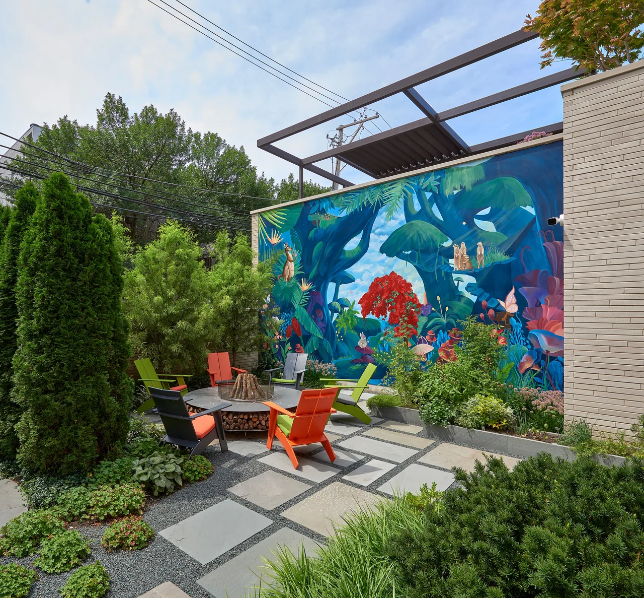 The outdoor patio features a colorful mural wall, mixed greenery, and a fire pit with vibrant seating arrangements.