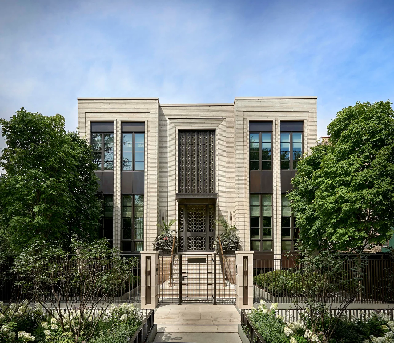 Front exterior of the Lakewood Residence featuring cream brick, tall black-framed windows, and symmetrical design with trees.