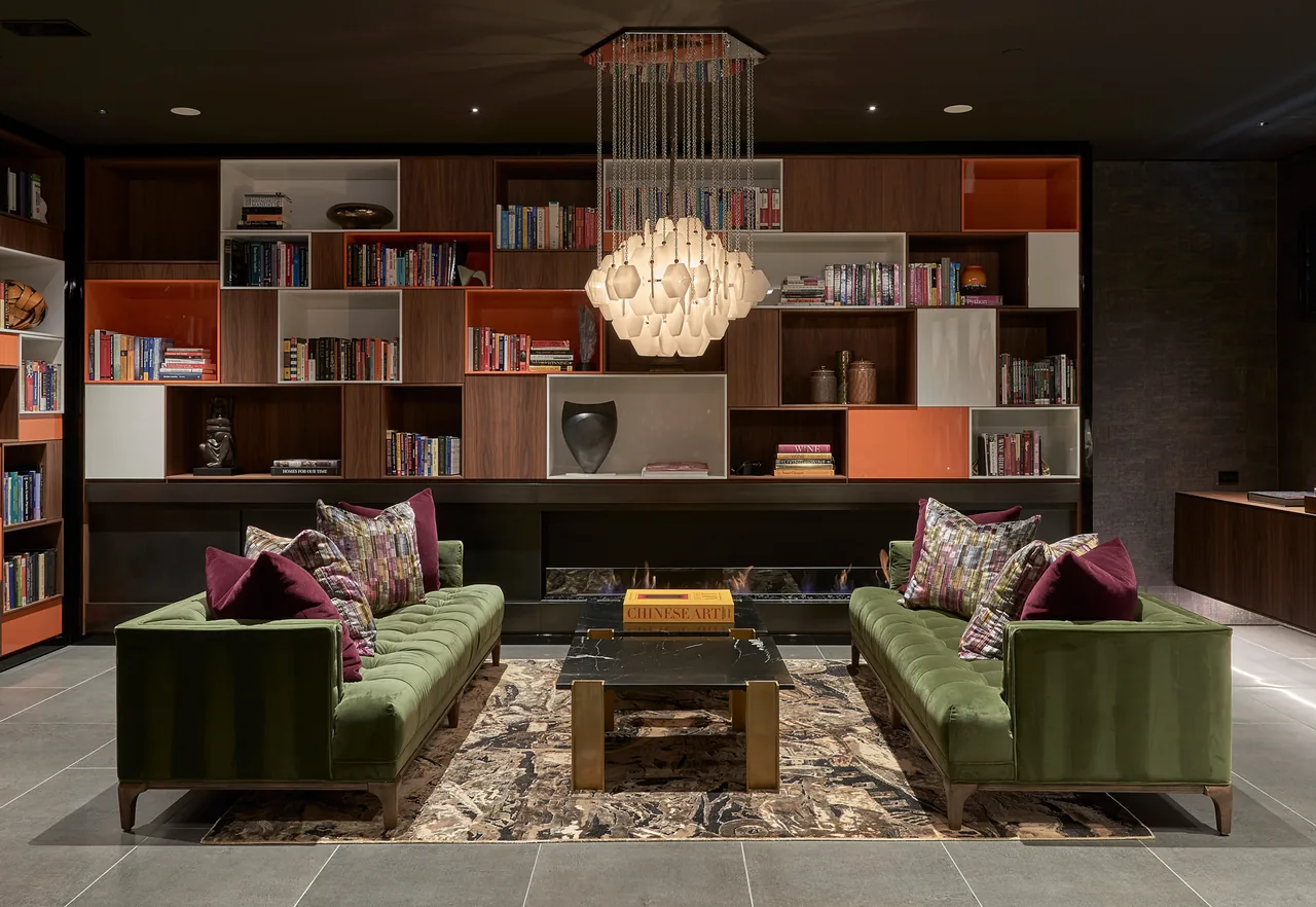 Living room features green velvet sofas, a built-in bookshelf with wood and orange panels, and a central chandelier above a black marble coffee table.