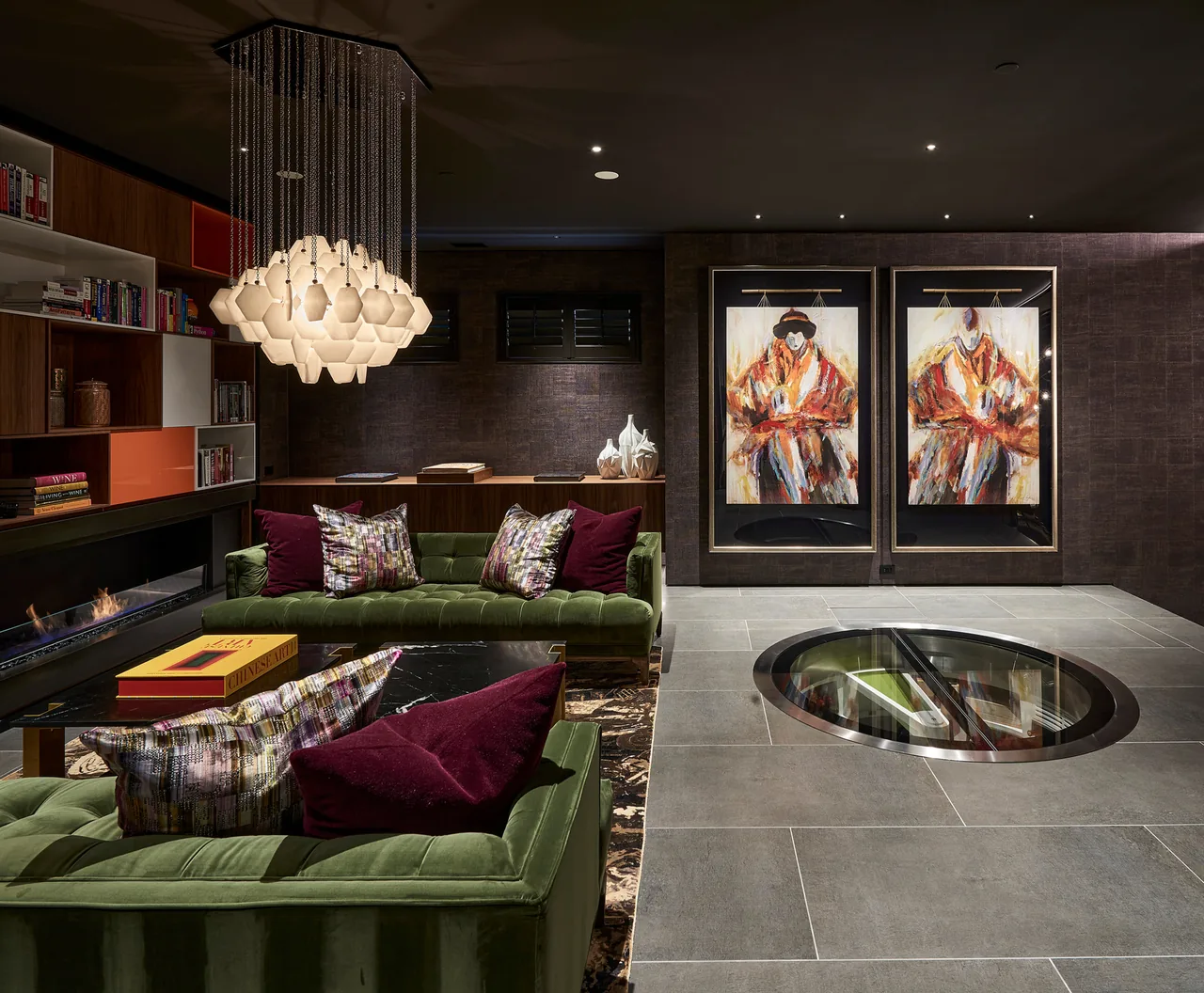 Interior living room features green velvet sofas, a modern pendant chandelier, built-in shelving, and a circular floor window.
