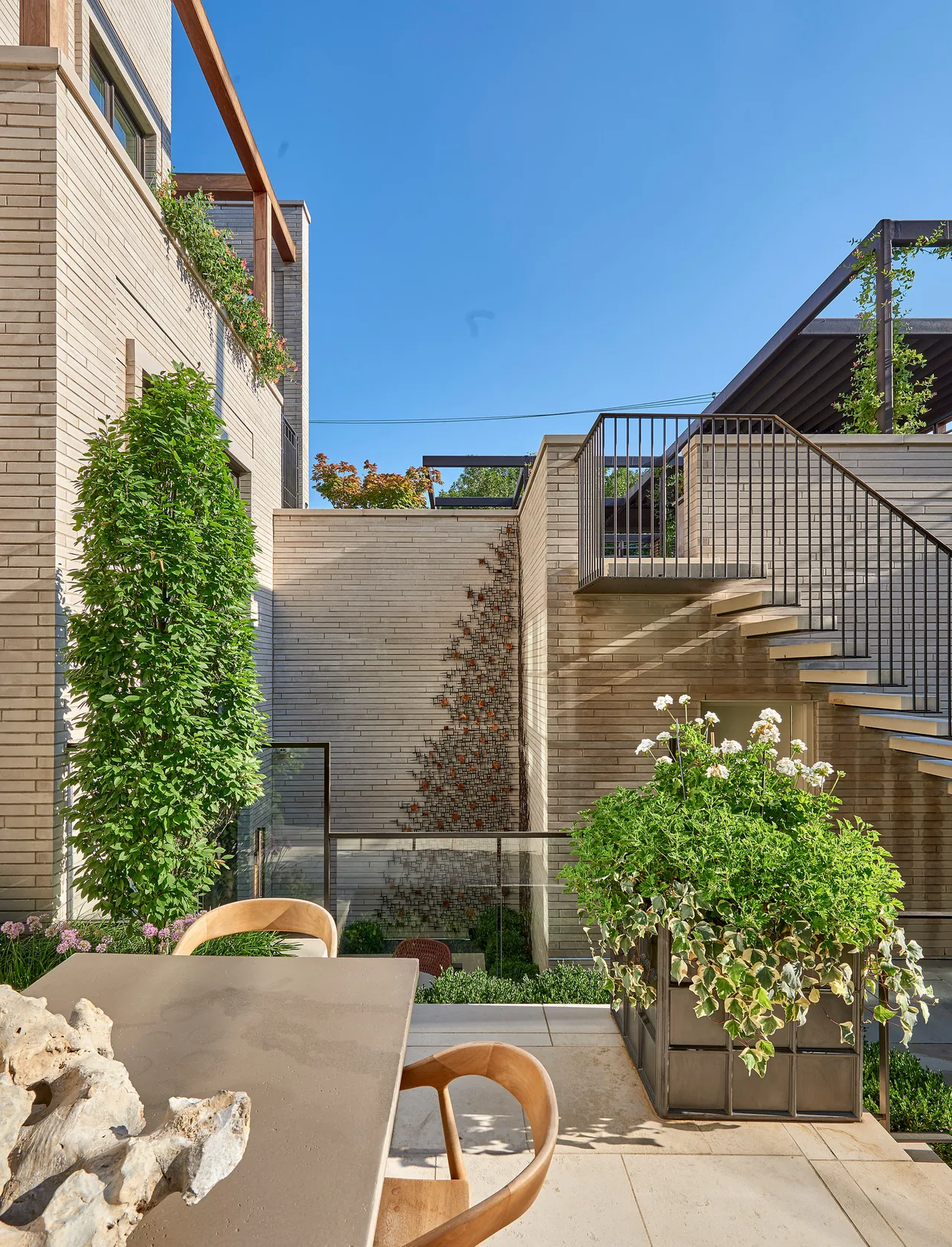 The exterior courtyard features a modern staircase with metal railing and abundant planting in a contemporary brick residence.
