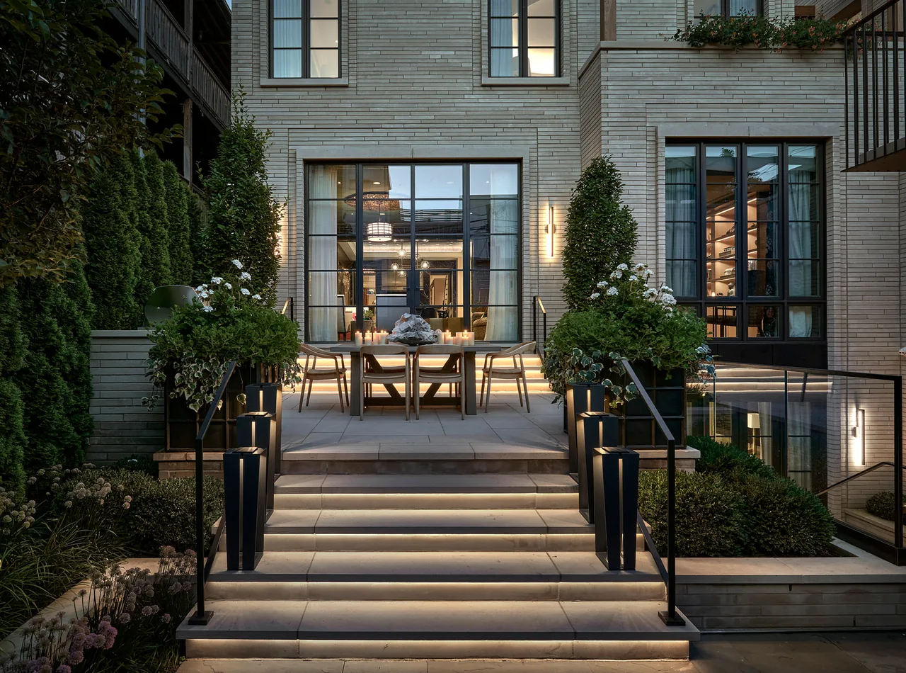 Lakewood Residence features a stone patio with integrated stair lighting and black-framed large grid windows facing the landscaped yard.