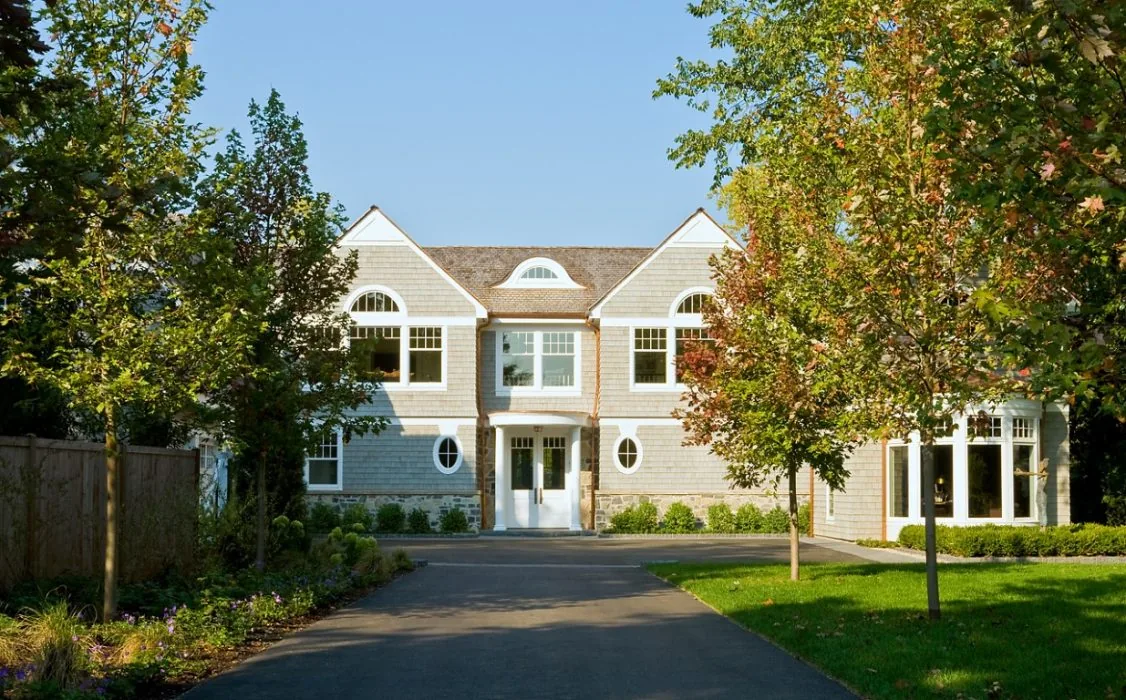 Two-story residence with shingle siding and symmetrical window design set back from a paved driveway.
