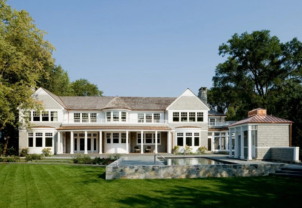 Back exterior of a two-story house with a covered porch and adjacent pool structure under a copper roof.