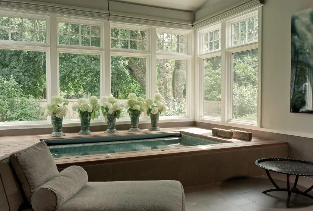 Indoor spa tub framed by large corner windows with multiple white flower vases on the ledge.