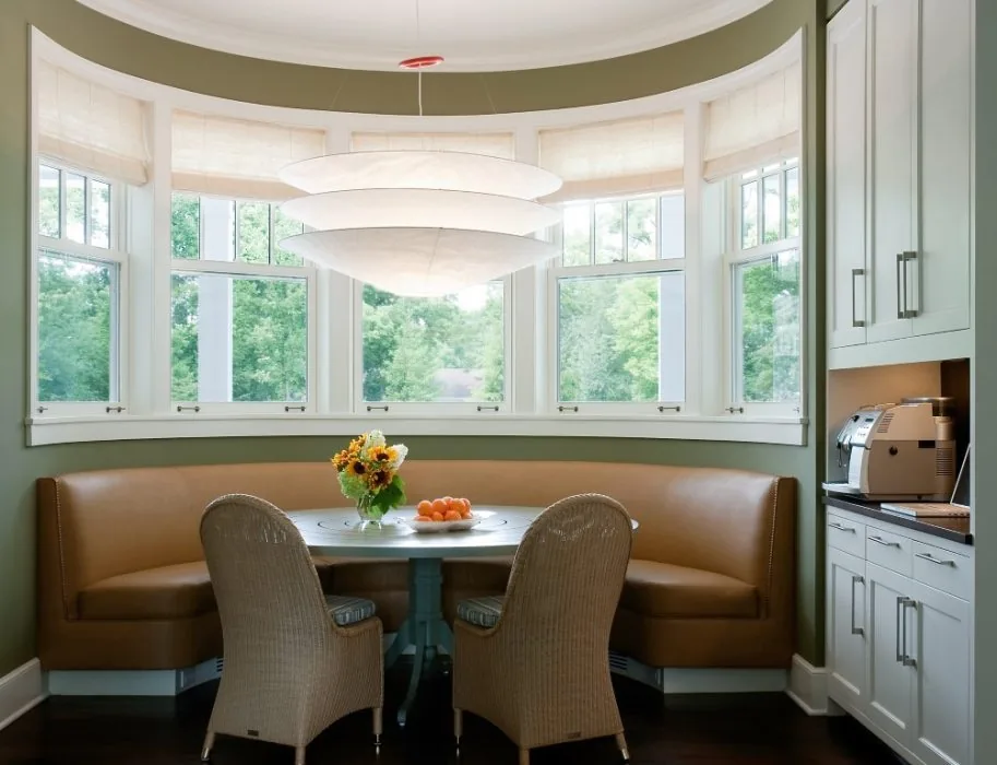 Breakfast nook with a curved leather bench, two wicker chairs, and a round table beneath a large layered pendant light by bay windows.