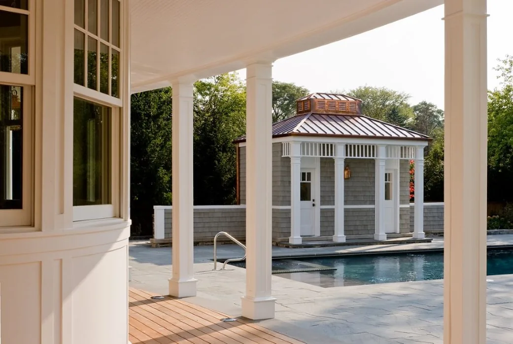 Poolside structure with copper roofing and white columns viewed from a covered porch at the getaway project.