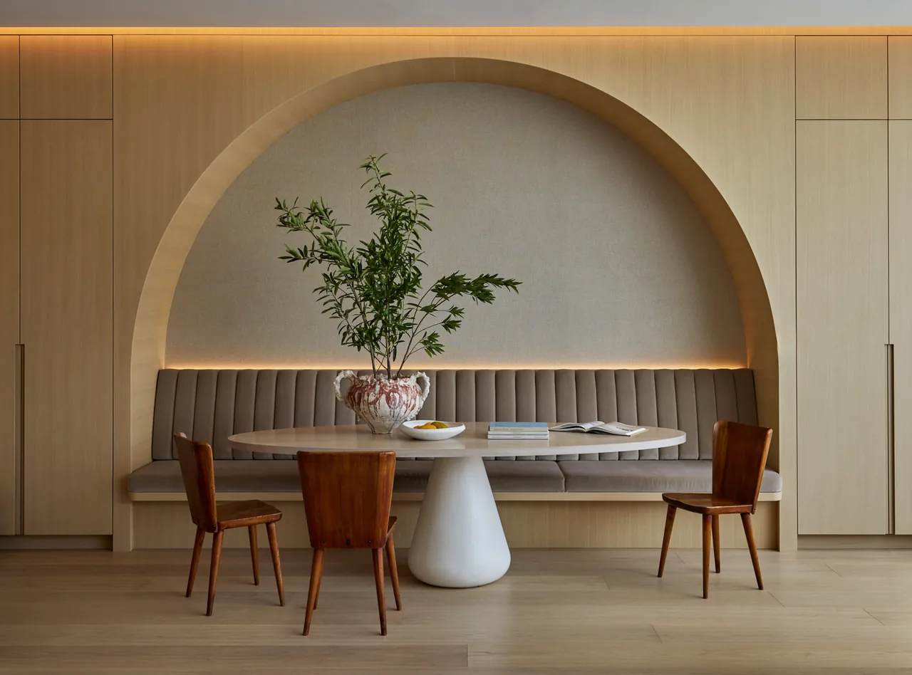 Dining area features built-in banquette seating under a wooden arch, a round table, and wooden chairs with a ceramic vase centerpiece.