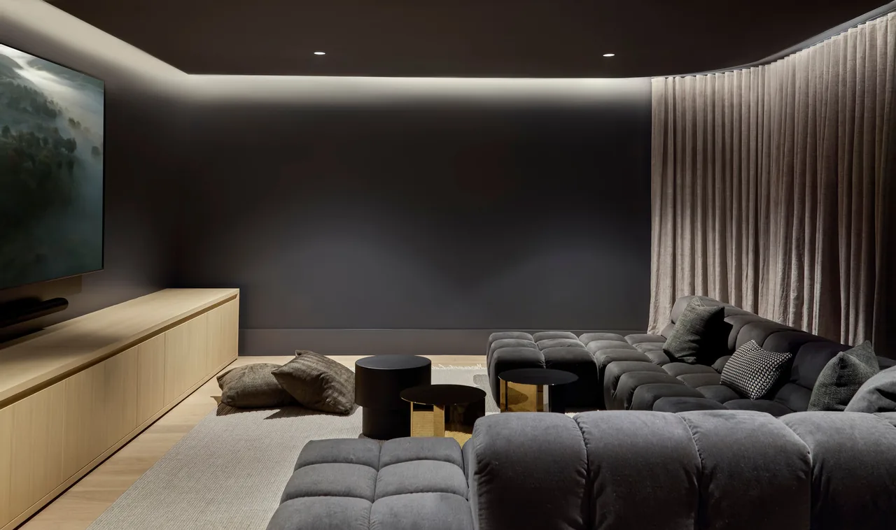 Living room featuring a large tufted sectional sofa, wall-mounted TV, and ambient lighting behind a wood-paneled media console.