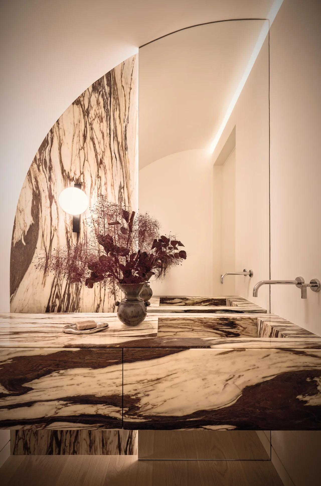 Howe Street bathroom features a striking marble vanity and wall-mounted faucets with an arched mirror.