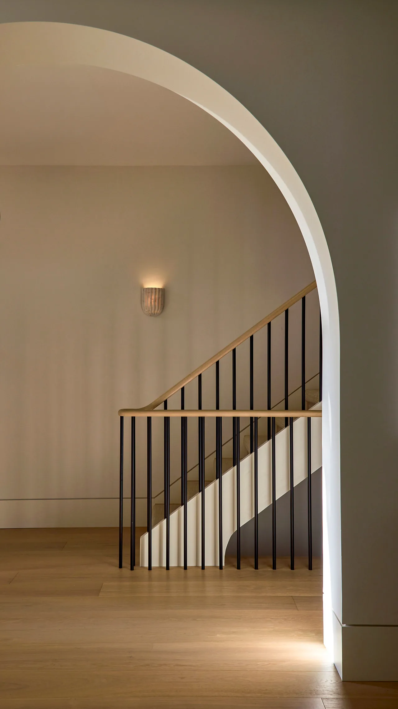 A staircase with black railing and light wood handrails viewed through a tall arched doorway.