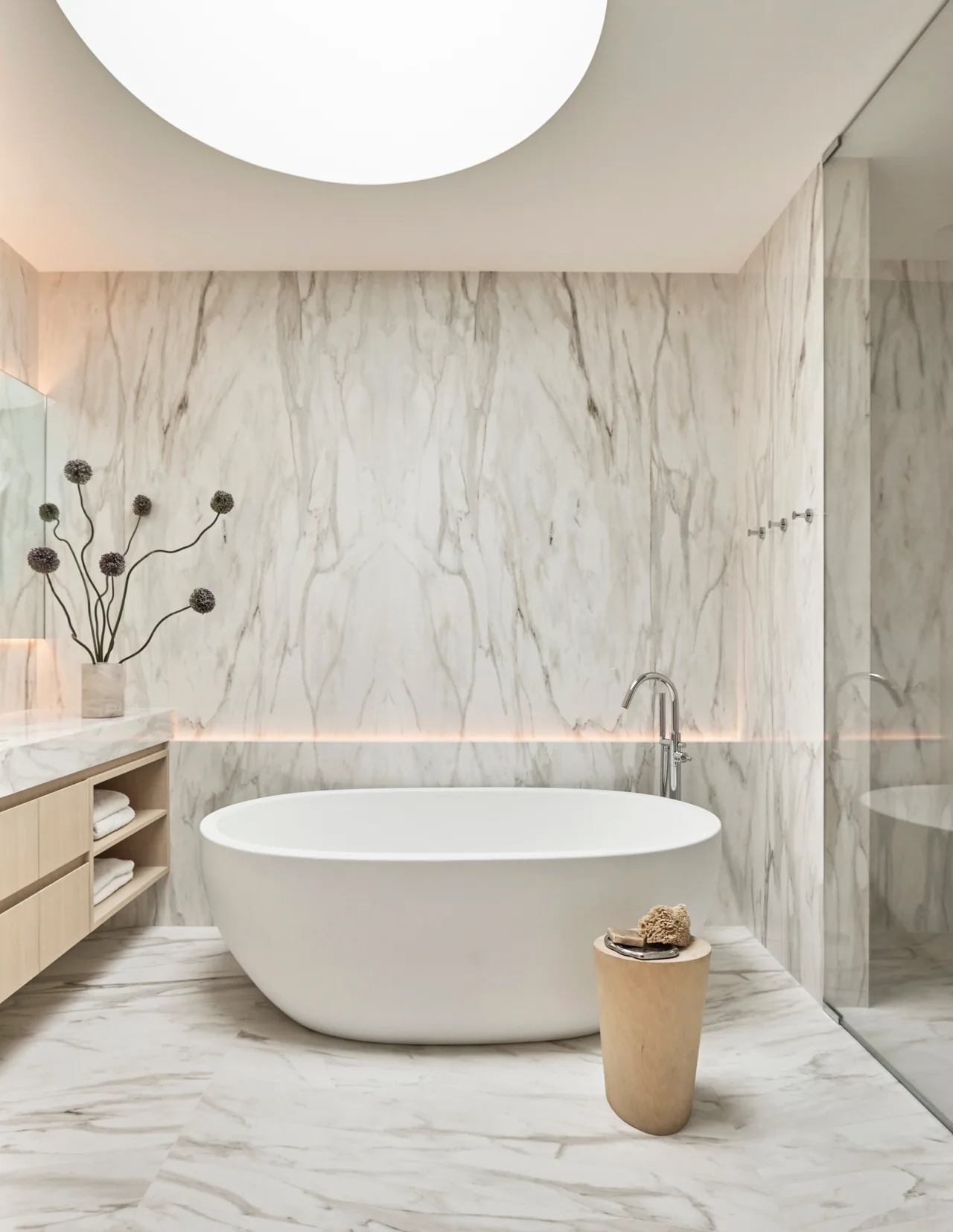 Bathroom featuring a freestanding tub under a circular skylight with marble wall and floor coverings.