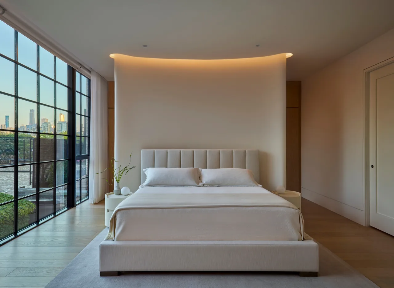 Howe Street bedroom features a tufted upholstered bed against a curved wall with soft indirect cove lighting and large black-framed windows.