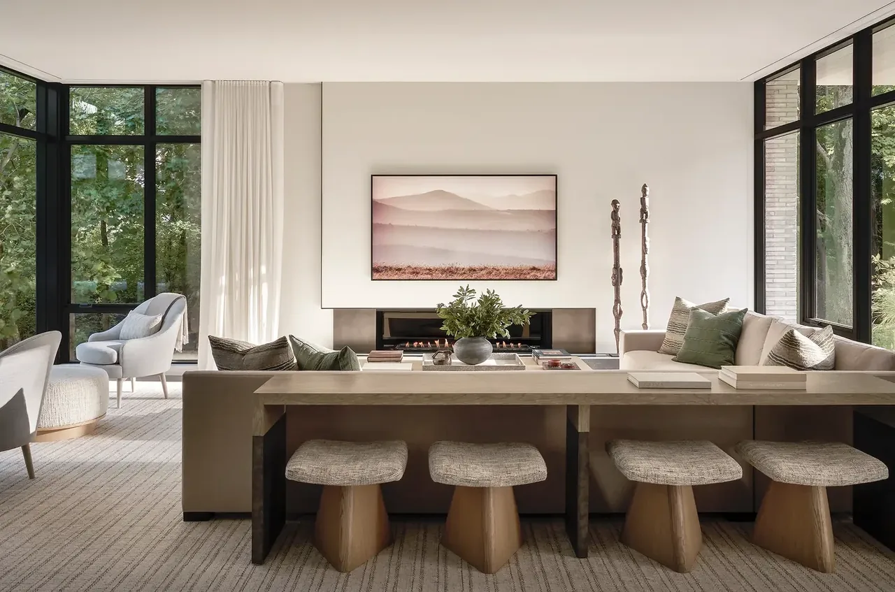 The Ravine Reimagined living room features large black window frames, a linear fireplace, and neutral tones.