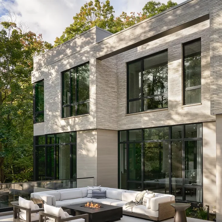 Exterior rear view of Ravine Reimagined featuring floor-to-ceiling glazing and a covered patio with modern outdoor furniture and fire pit.