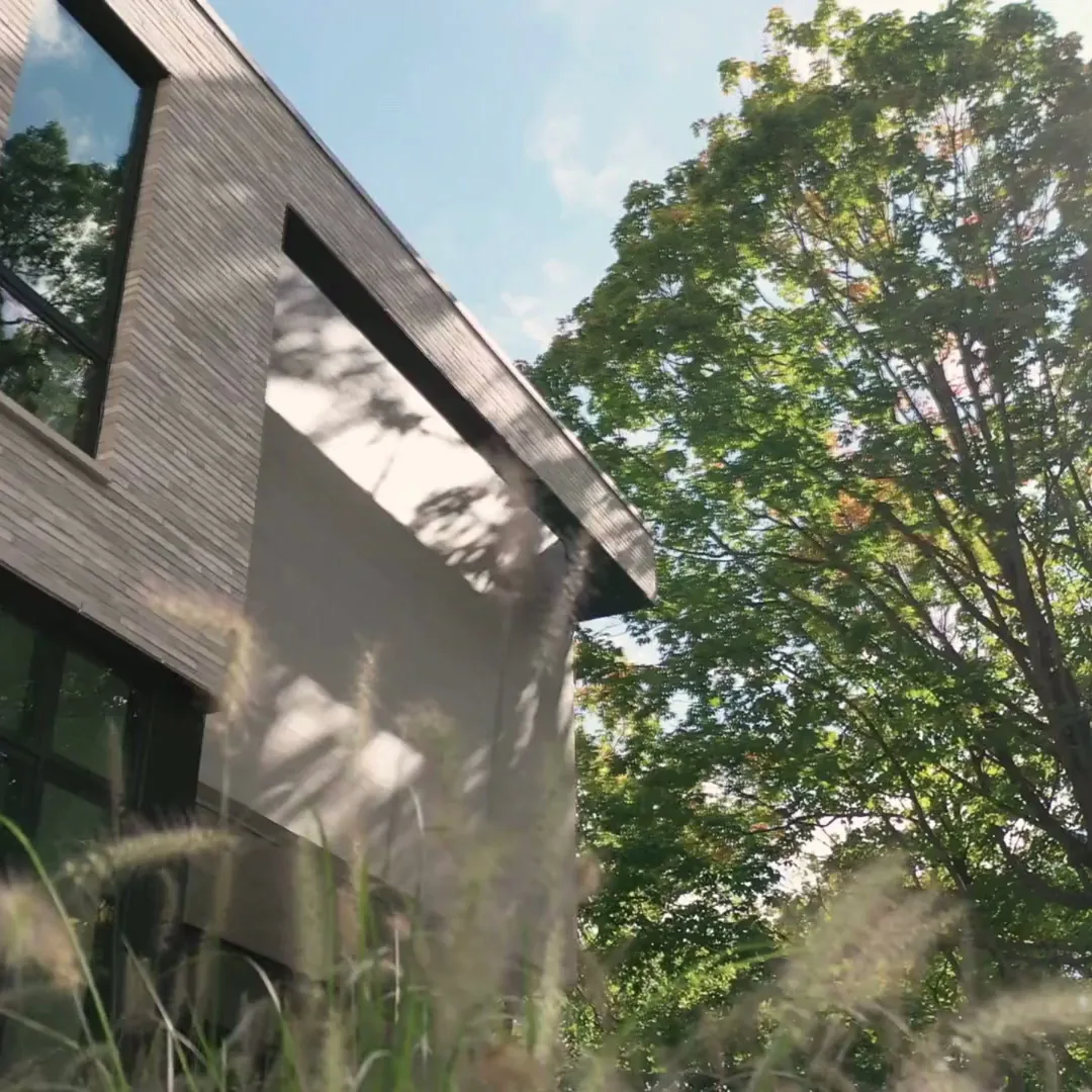 The Ravine Reimagined project highlights horizontal wood siding and large black-framed windows on a modern home's exterior.