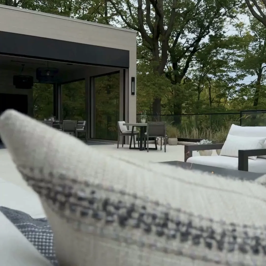 Contemporary outdoor living space with seating and dining areas opening to a natural leafy backdrop.