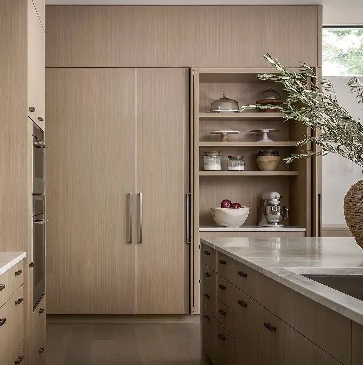 Light wood kitchen cabinetry with built-in appliances and open shelving beside a marble-topped island.