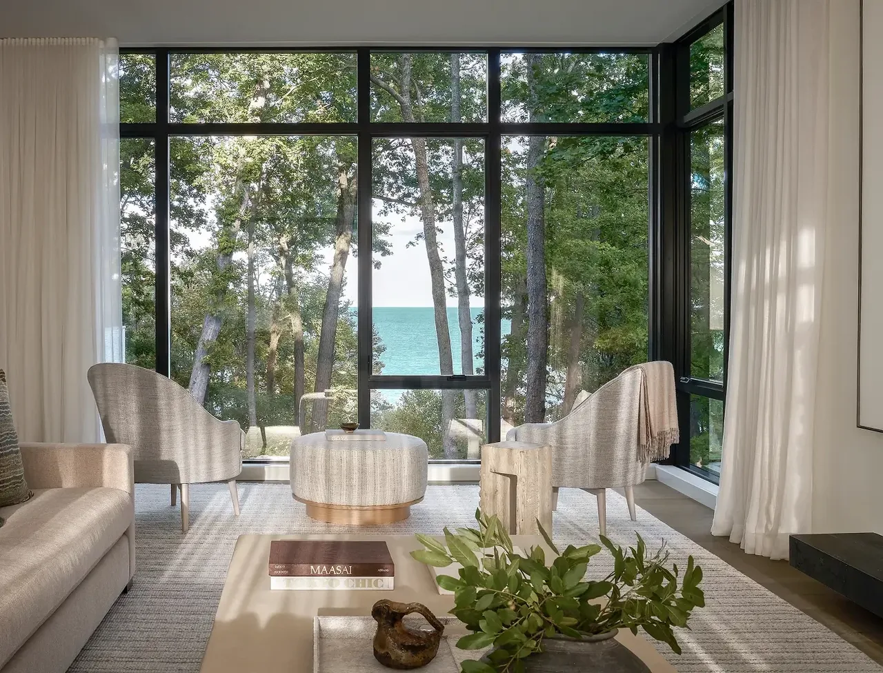 Living room features large black-framed floor-to-ceiling windows with views of trees and water in Ravine Reimagined project.