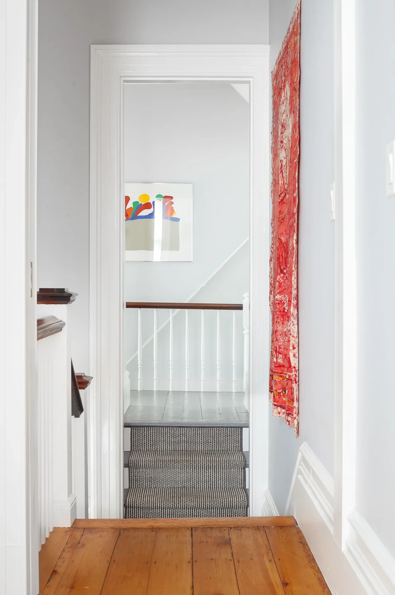 Interior hallway view showing wood flooring, a staircase with patterned carpet runner, and colorful wall art.