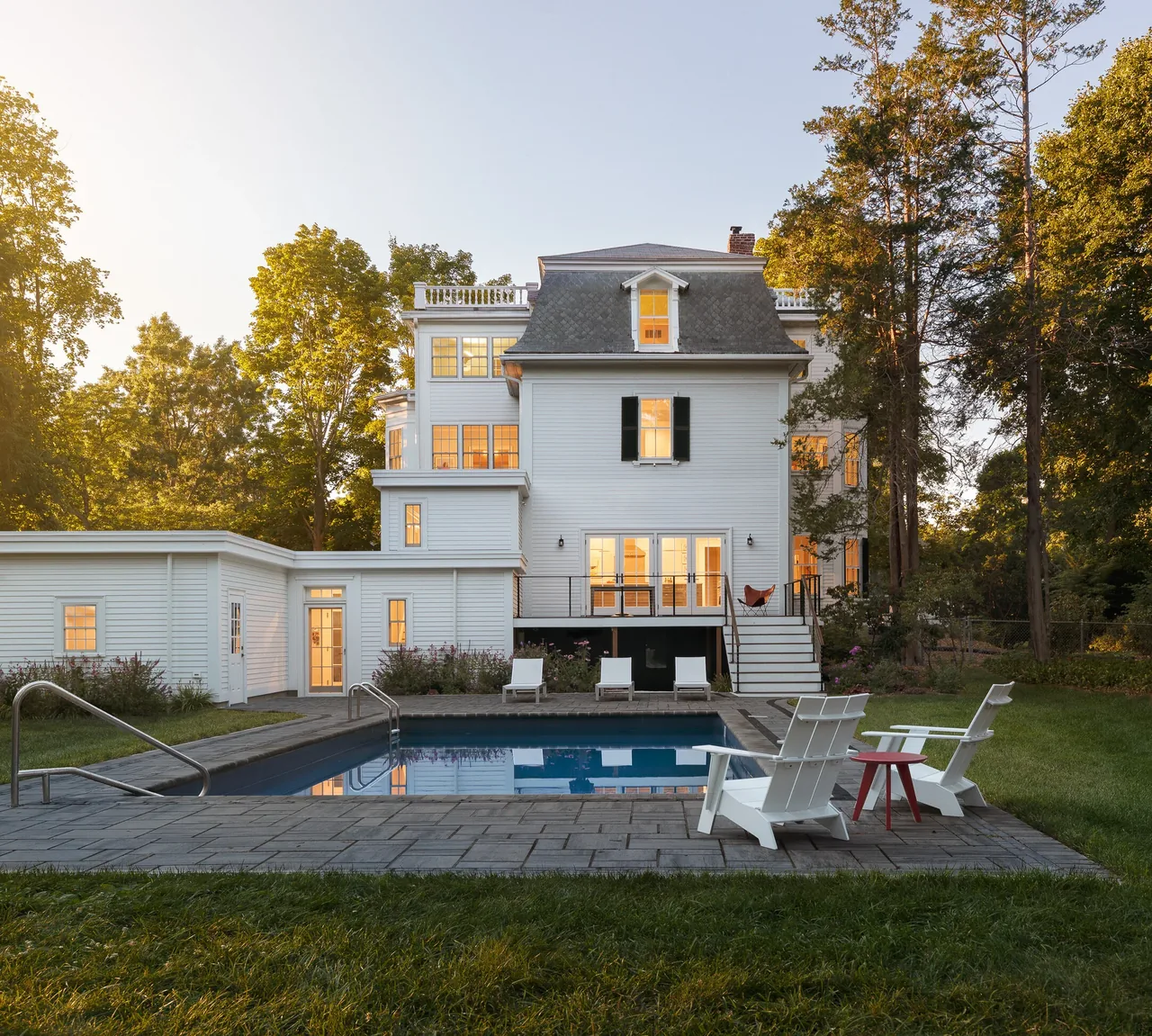 Rear exterior view of a white Federal-style house with a pool and patio seating in its backyard.