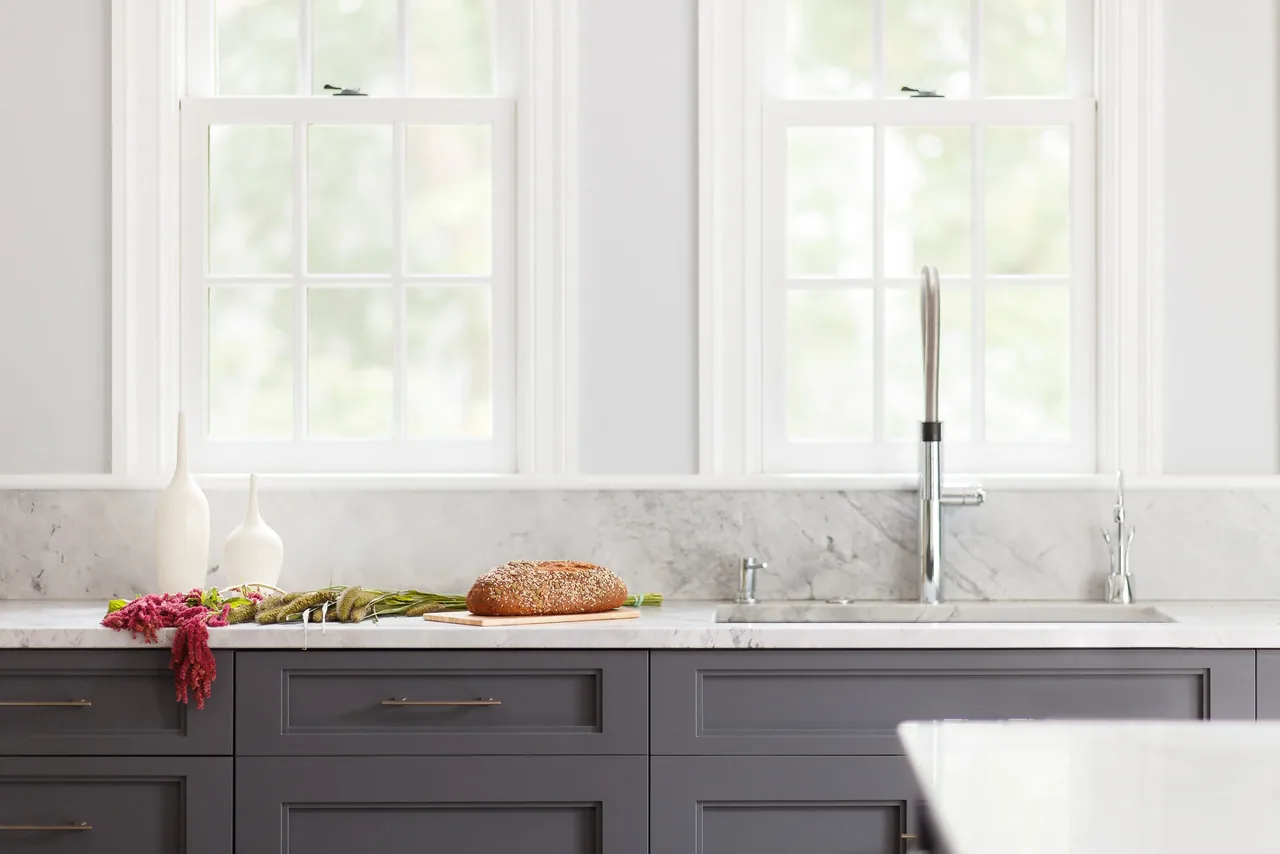 Kitchen countertop with gray cabinets and two large windows providing natural daylight.