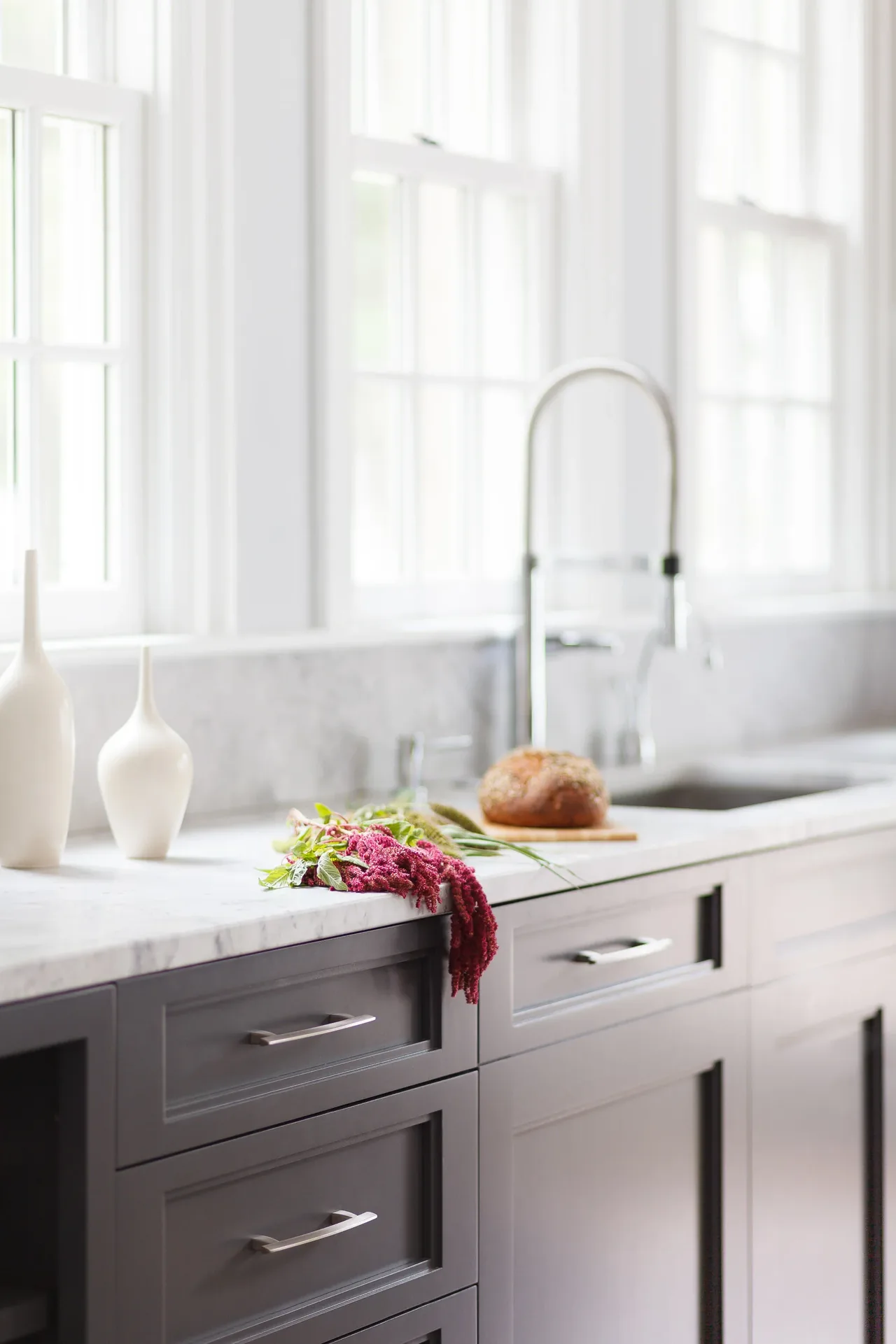Kitchen countertop with marble surface and gray cabinetry under natural light from windows.