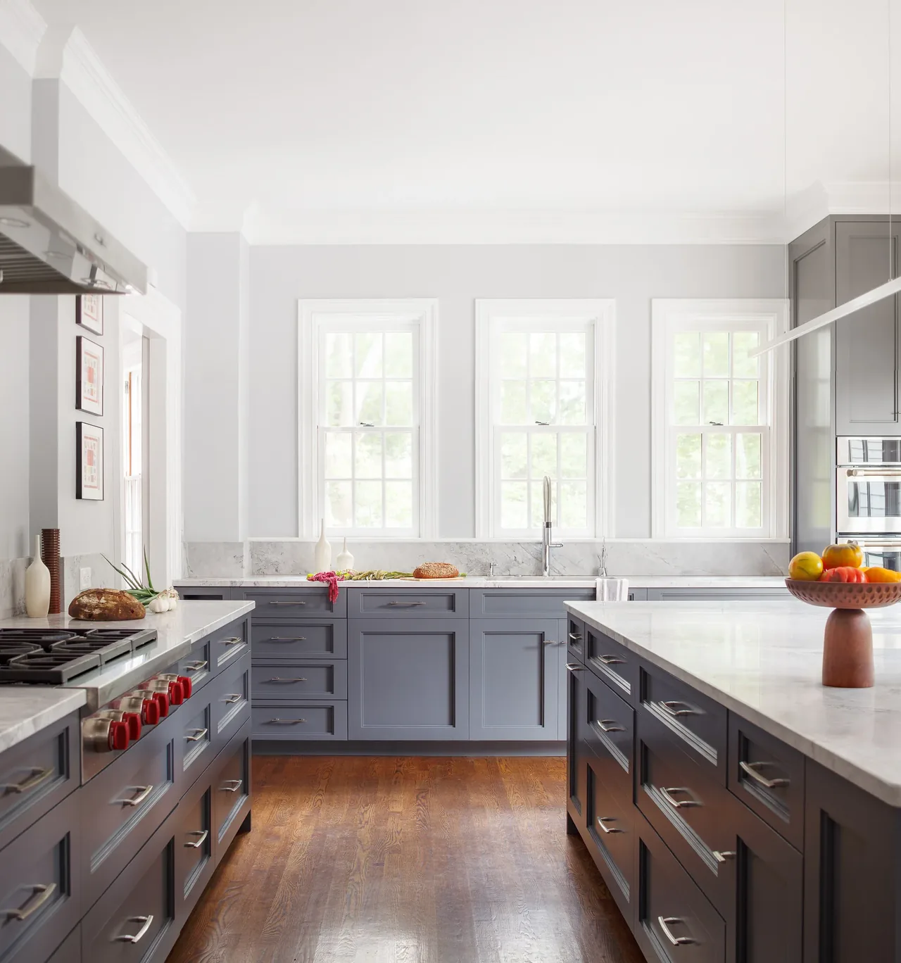 Kitchen featuring gray cabinetry with marble countertops and backsplash, illuminated by natural light from three windows.