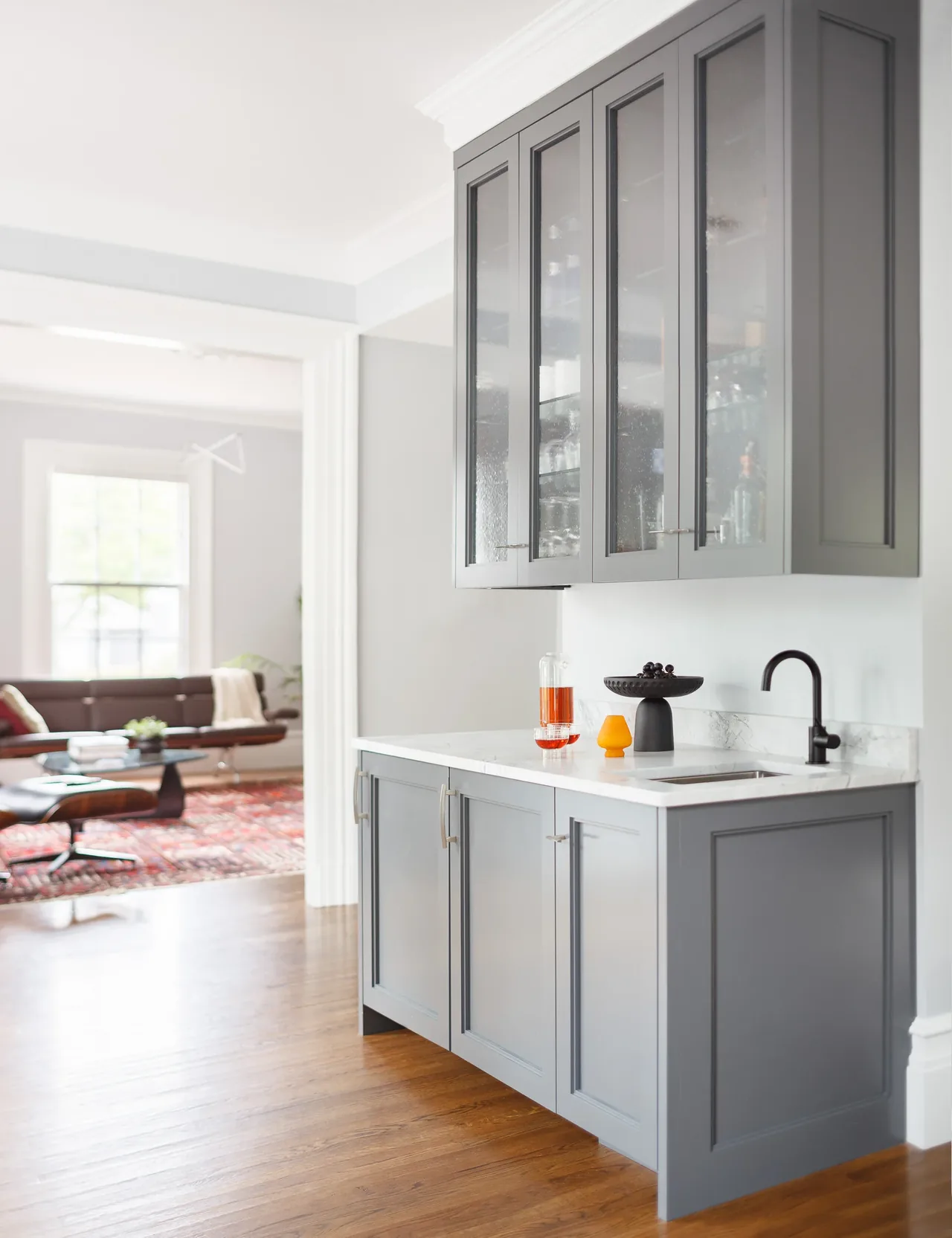 Gray cabinetry with marble countertop and black faucet in a kitchen area adjacent to a living room.