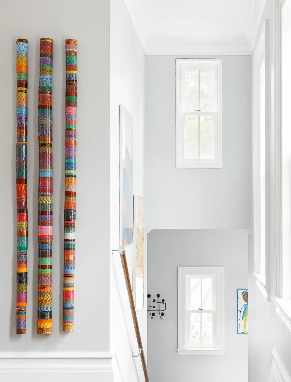 The stairwell features two white-framed windows and colorful vertical art on the white wall.