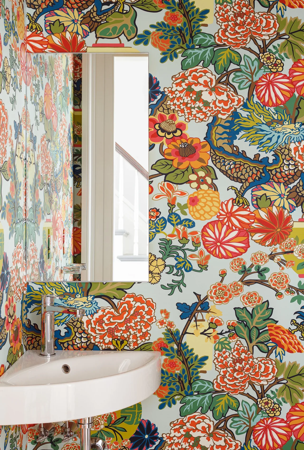 Bathroom corner featuring a white wall-mounted sink with a chrome faucet, a rectangular mirror, and vivid floral wallpaper.
