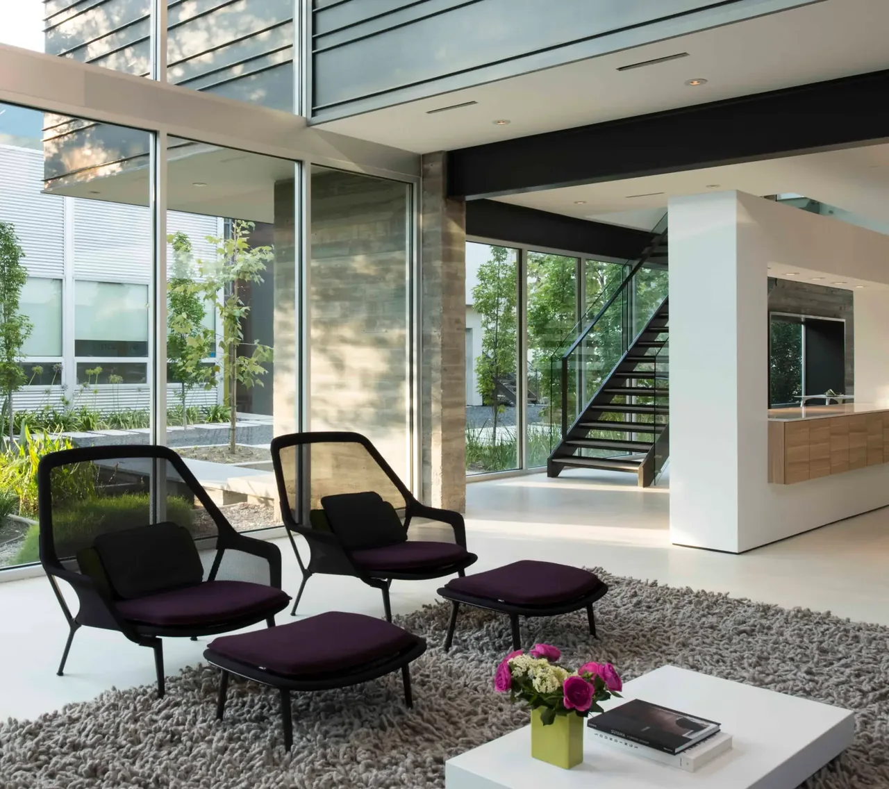 Living room in Jade house features black-framed mesh chairs and large floor-to-ceiling windows with concrete steps visible outside.