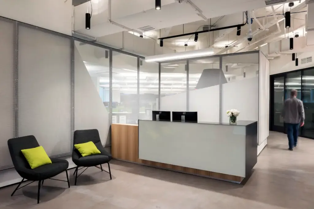 Modern reception desk area with seating and visible workspace behind glass walls.