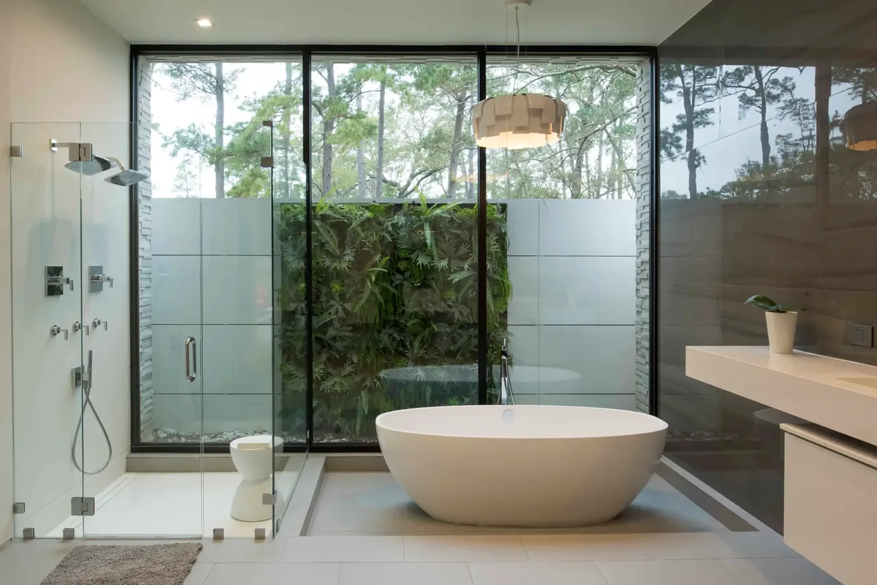 Bathroom features a freestanding tub and a glass-enclosed shower with large windows providing a view of an exterior green wall.