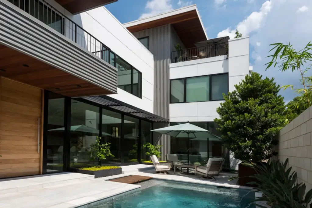 Jade house features black window frames and a patio area with seating and umbrella beside a pool.