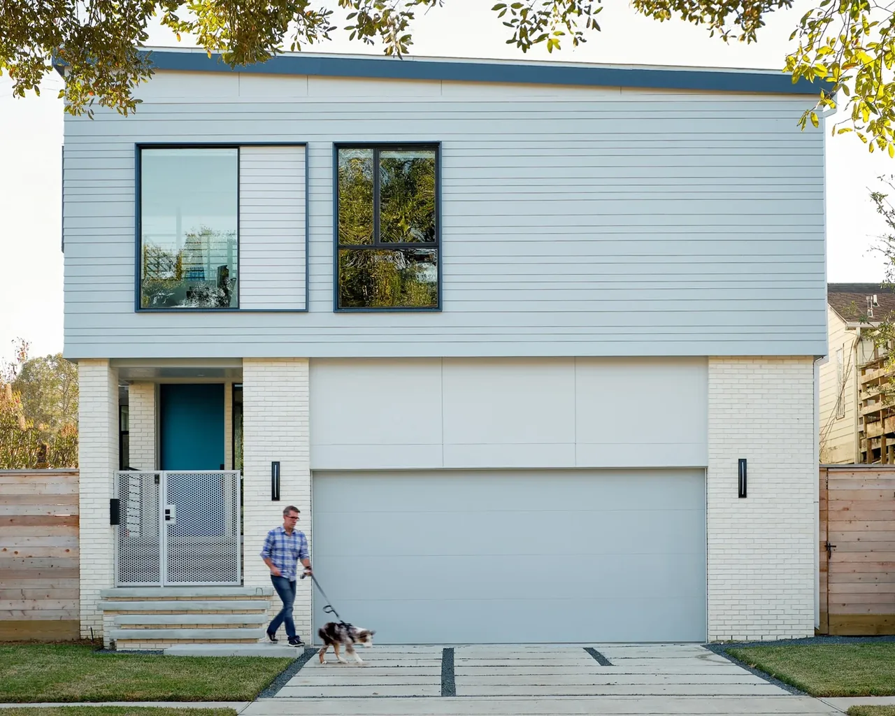 The Windemere Residence features a combination of white brick and horizontal siding with large black-framed windows on the upper level.