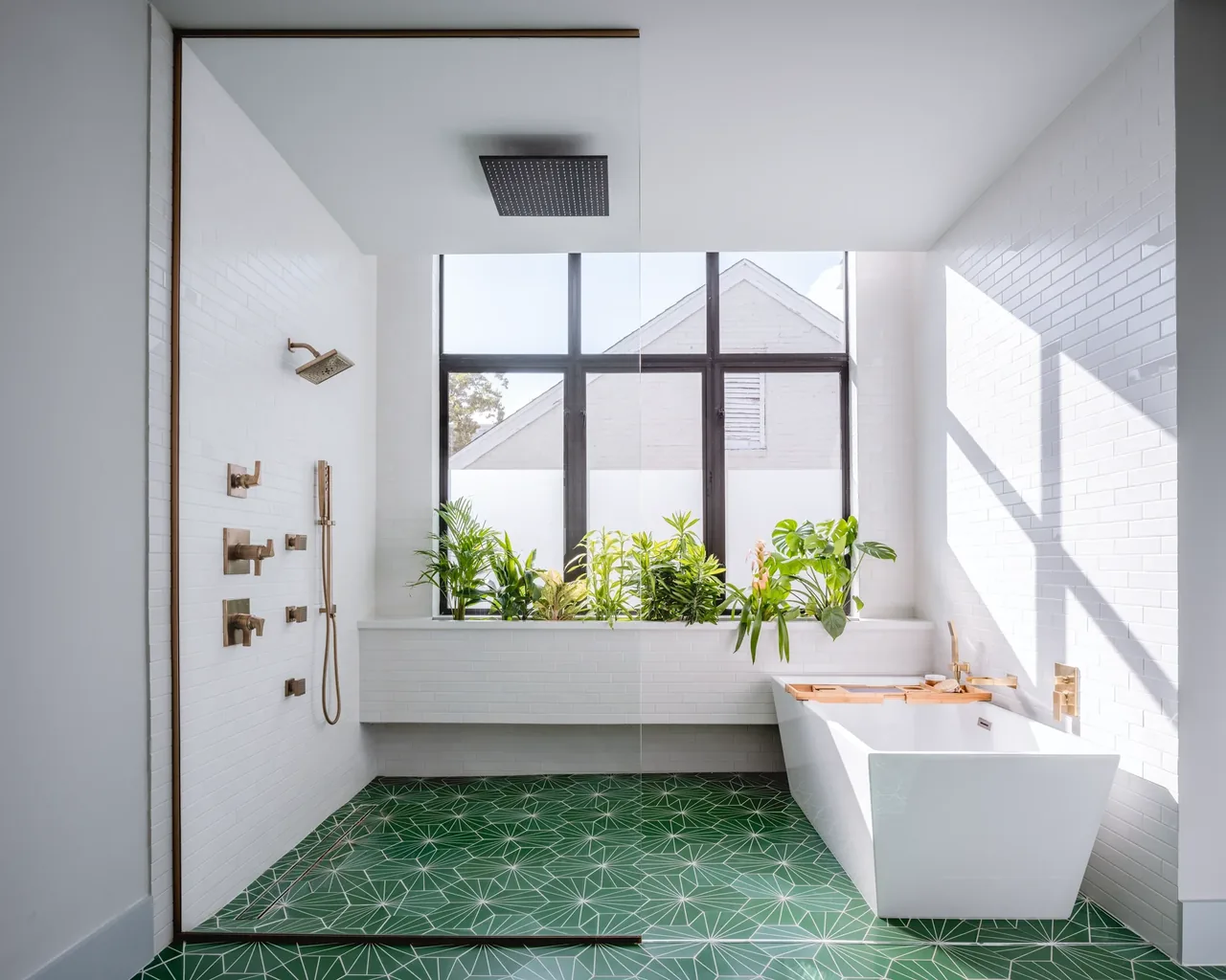 The Windemere Residence bathroom features a freestanding tub, walk-in shower, brass fixtures, and green geometric floor tiles with a large window sill planters.