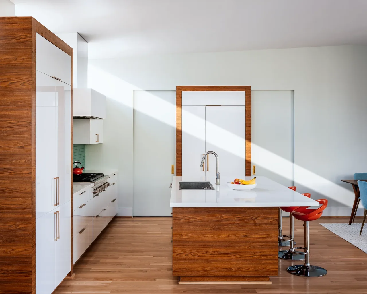 The Windemere Residence kitchen features a white island with wooden panels and bright red bar stools.