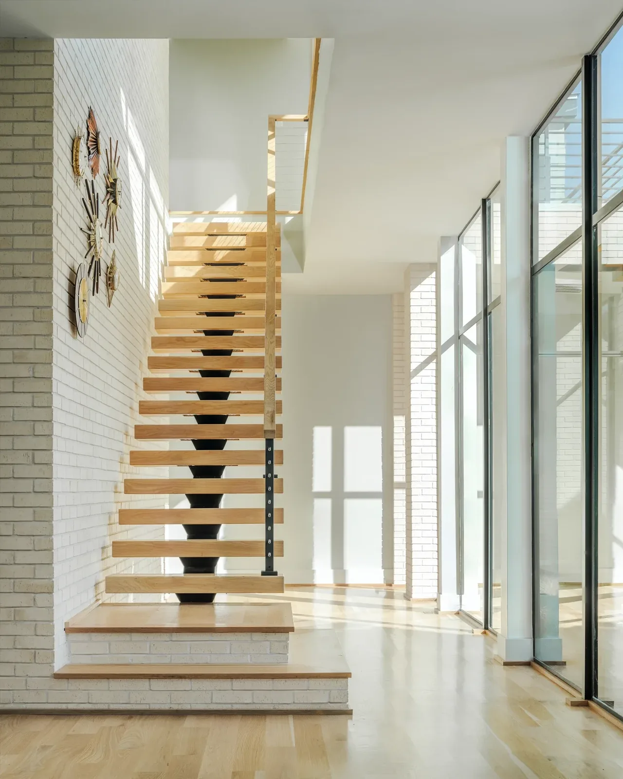 Floating wood staircase with metal central support by floor-to-ceiling windows in the Windemere Residence.