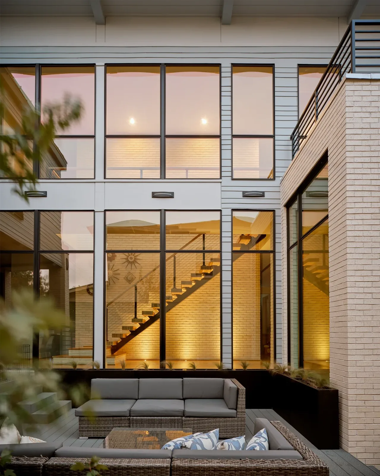 Windemere Residence features large black window frames and an outdoor seating area under soft lighting.