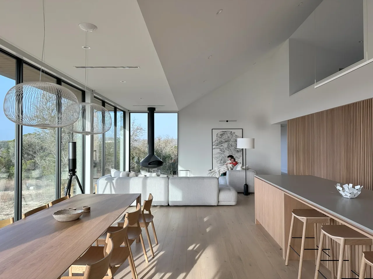 Open-plan living and dining room with floor-to-ceiling glazing and black window frames at the Wimberley Residence.