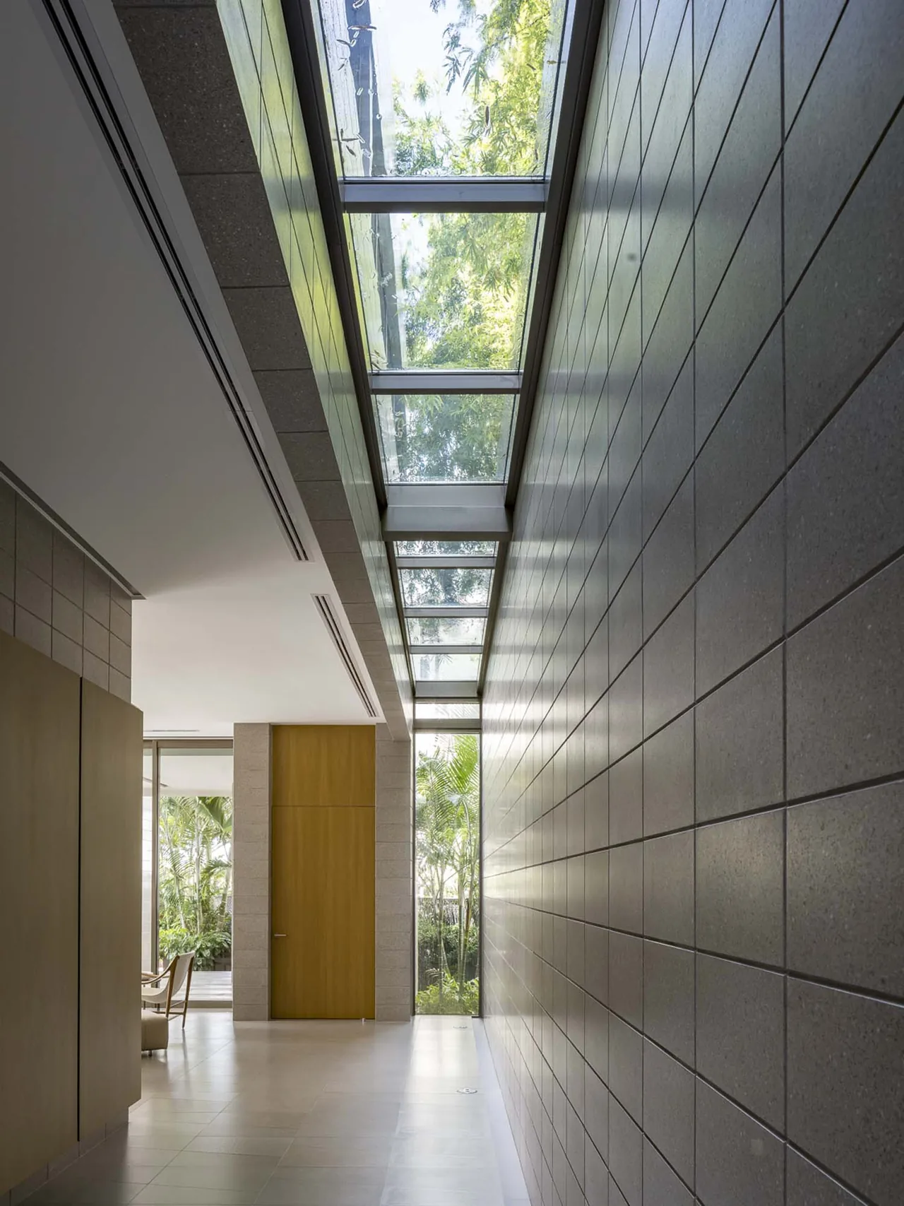 Narrow corridor with textured tiled walls and a skylight ceiling showing tree views in Intracoastal Residence.