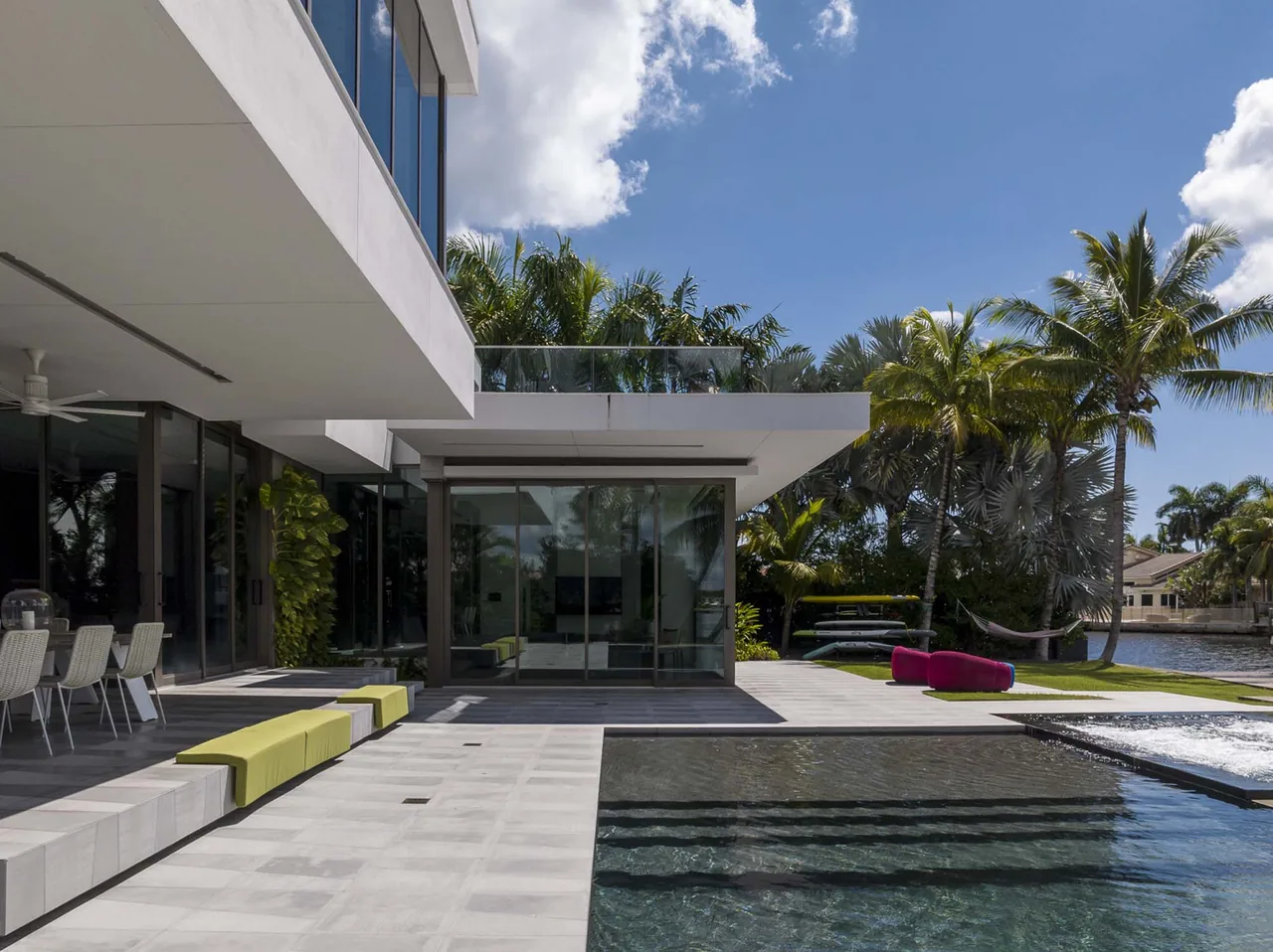 The Intracoastal Residence features a poolside patio with seating and large windows overlooking tropical landscaping.