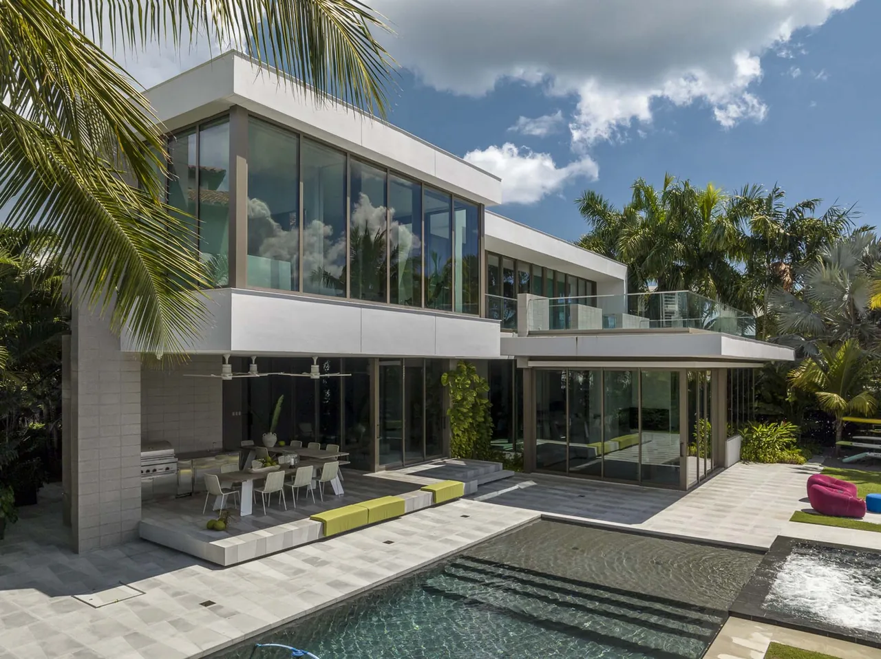 The Intracoastal Residence features large glass windows, an outdoor dining patio with built-in bench seating, and a pool area with tropical landscaping.