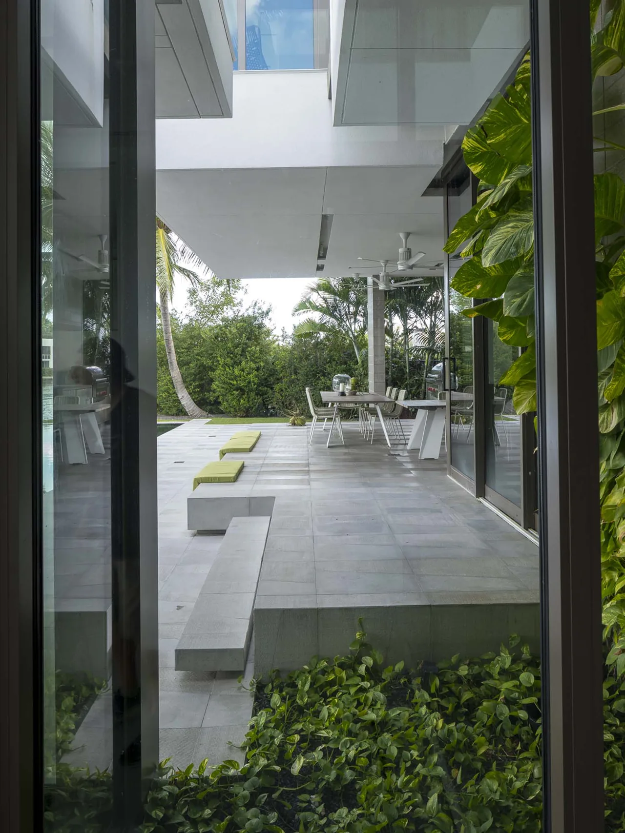 Outdoor patio at Intracoastal Residence with dining area, concrete flooring, built-in bench, and lush greenery.