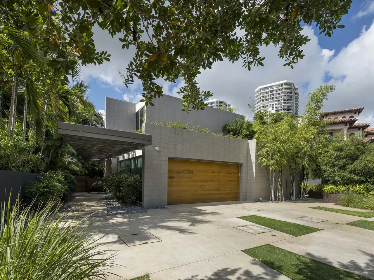 Intracoastal Residence features a modern design with a concrete facade, wood garage door, and metal canopy.