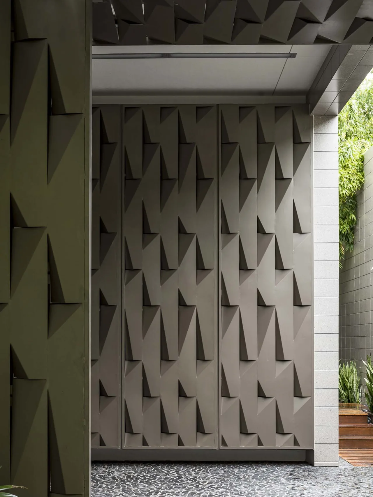 Exterior wall detail featuring geometric textured panels with angular shadows and natural stone pebble flooring at Intracoastal Residence.