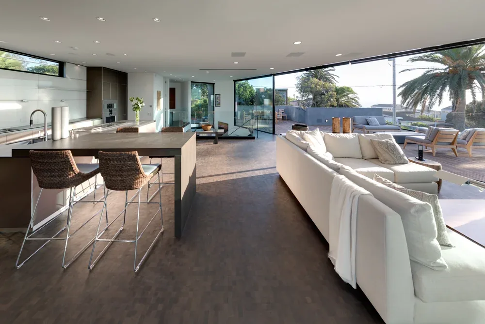 Open living room and kitchen with expansive glass walls and outdoor lounge seating at Neptune House.