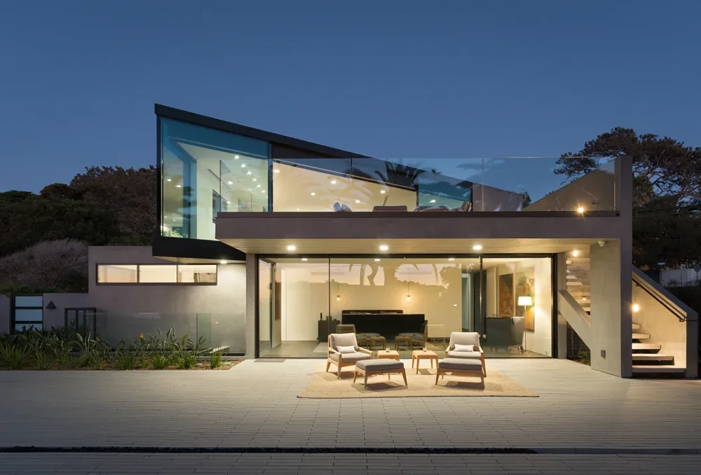 Neptune House features expansive glass walls and a cantilevered second floor with an outdoor seating area on the patio.