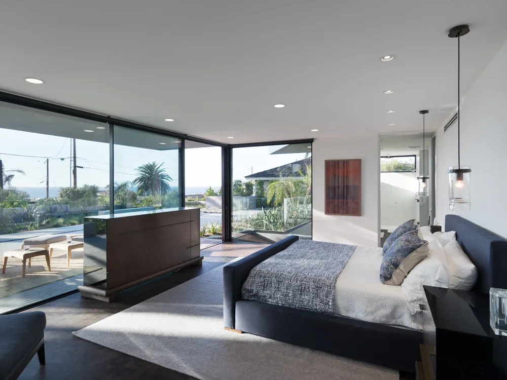 Neptune House bedroom with floor-to-ceiling corner windows providing an ocean view and natural light.